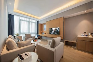 Una habitación de hotel moderna con un conjunto de sofás, una mesa de comedor, un televisor de pantalla plana montado en la pared y una pequeña cocina.