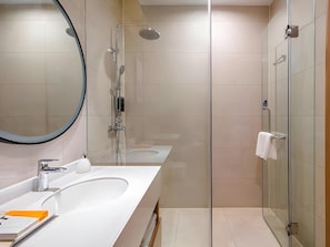 A modern bathroom with a large mirror, two sinks, a shower, and a glass-enclosed shower area. - Kyriad Marvelous Hotel (Guangzhou)