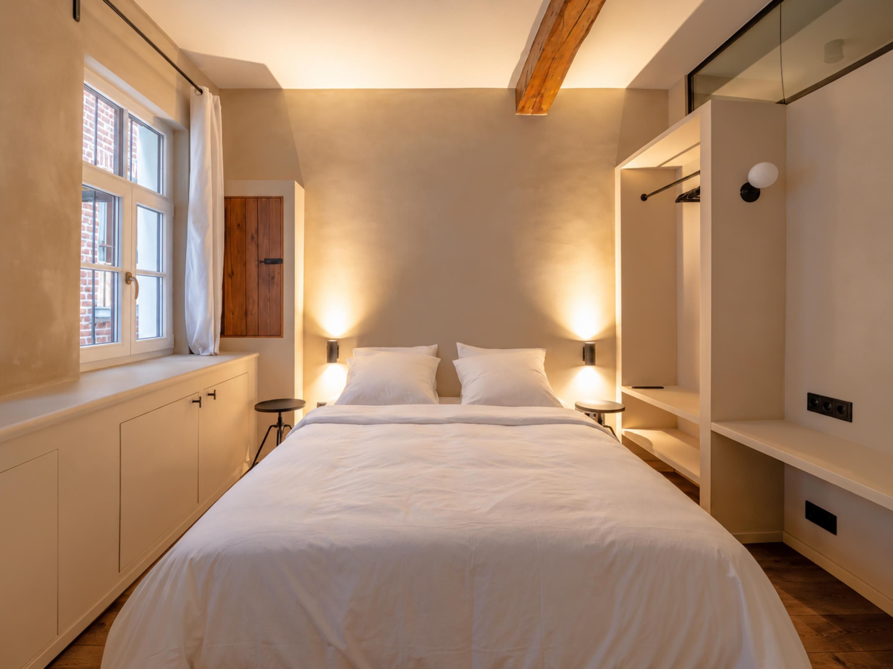 A modern bedroom with a large bed, bedside tables, a wardrobe, and a window with curtains.