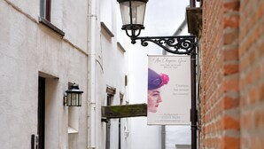 A narrow alley with a sign for 'Au Chateau Gris' boutique, a white building with a brick wall, and a hanging street lamp. - Le Sablon Retreat Private En Suite Room (Brussels)