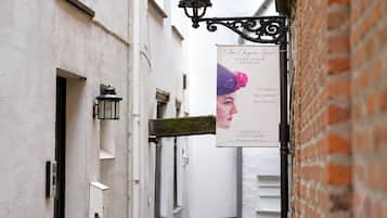 A narrow alley with a sign for 'Au Chateau Gris' boutique, a white building with a brick wall, and a hanging street lamp.
