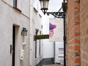 A narrow alley with a sign for 'Au Chateau Gris' boutique, a white building with a brick wall, and a hanging street lamp. - Le Sablon Retreat Private En Suite Room (Brussels)