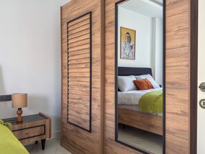 A bedroom with a wooden wardrobe, a bedside table with a lamp, and a bed with pillows. - Qoople Elize C15 - Cozy 1-bedroom apartment in Alanya (Alanya)