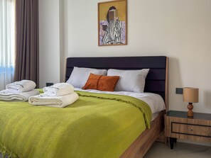 Una cama bien hecha con una manta verde, dos almohadas y toallas dobladas.