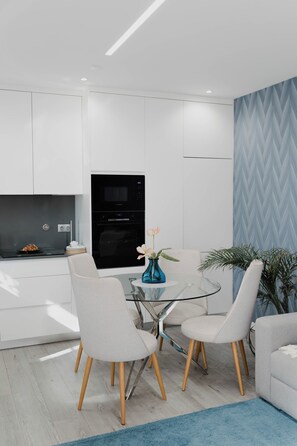A modern kitchen with white cabinetry, a Bosch microwave, and a dining area with a glass table and four chairs. - Casa da Venda by Lethes Legacy (Refóios do Lima)