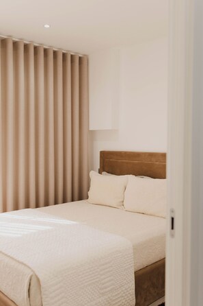 Quarto de hotel com cama, cortinas, cabeceira e luminária fixada na parede.
