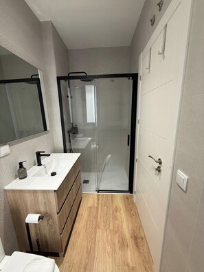 A bathroom with a wooden vanity, a glass shower enclosure, and a white door. - Aires de Salamanca Calixto (Salamanca)