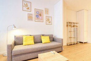 A living room with a grey sofa, two yellow cushions, a floor lamp, and a coffee table. There are framed artworks on the wall and a white wardrobe with a hanging rack. - AT Arriba 5 - University B Center (Salamanca)