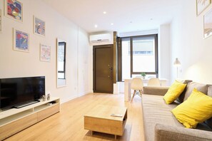A modern living room with a flat-screen TV, a wooden coffee table, a sofa with yellow cushions, and a dining area with a table and chairs. - AT Arriba 5 - University B Center (Salamanca)