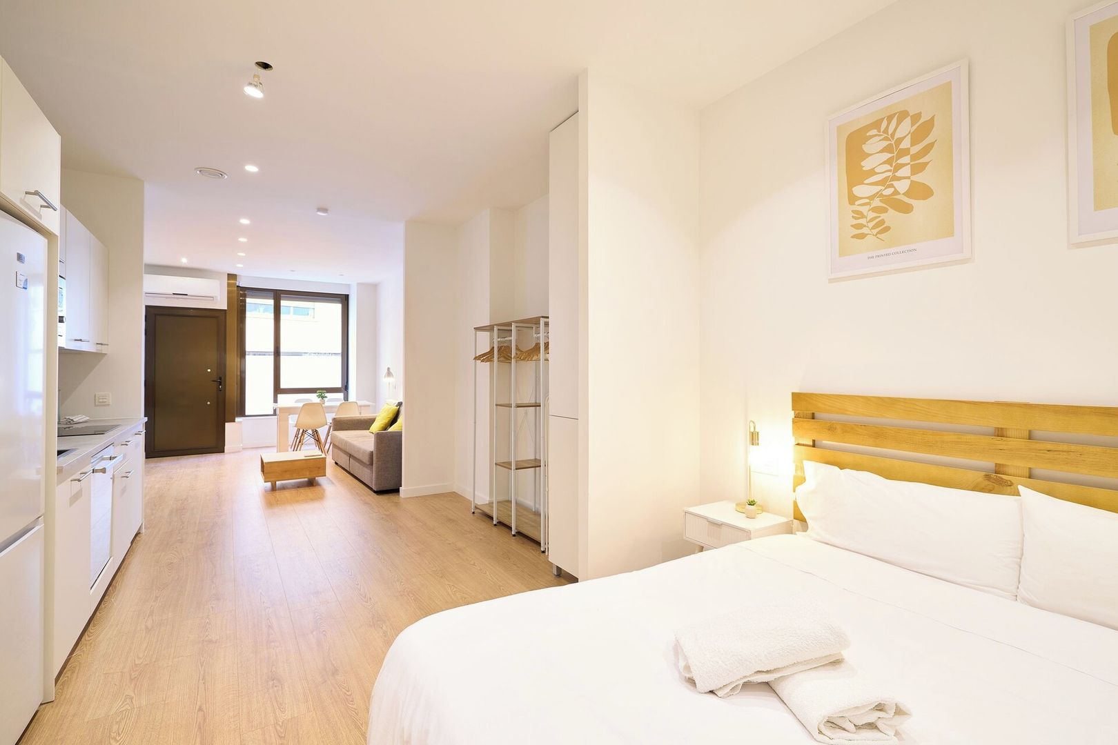 A hotel room with a bed, bedside table, and a wardrobe. There is a sofa and a dining table in the adjacent room.