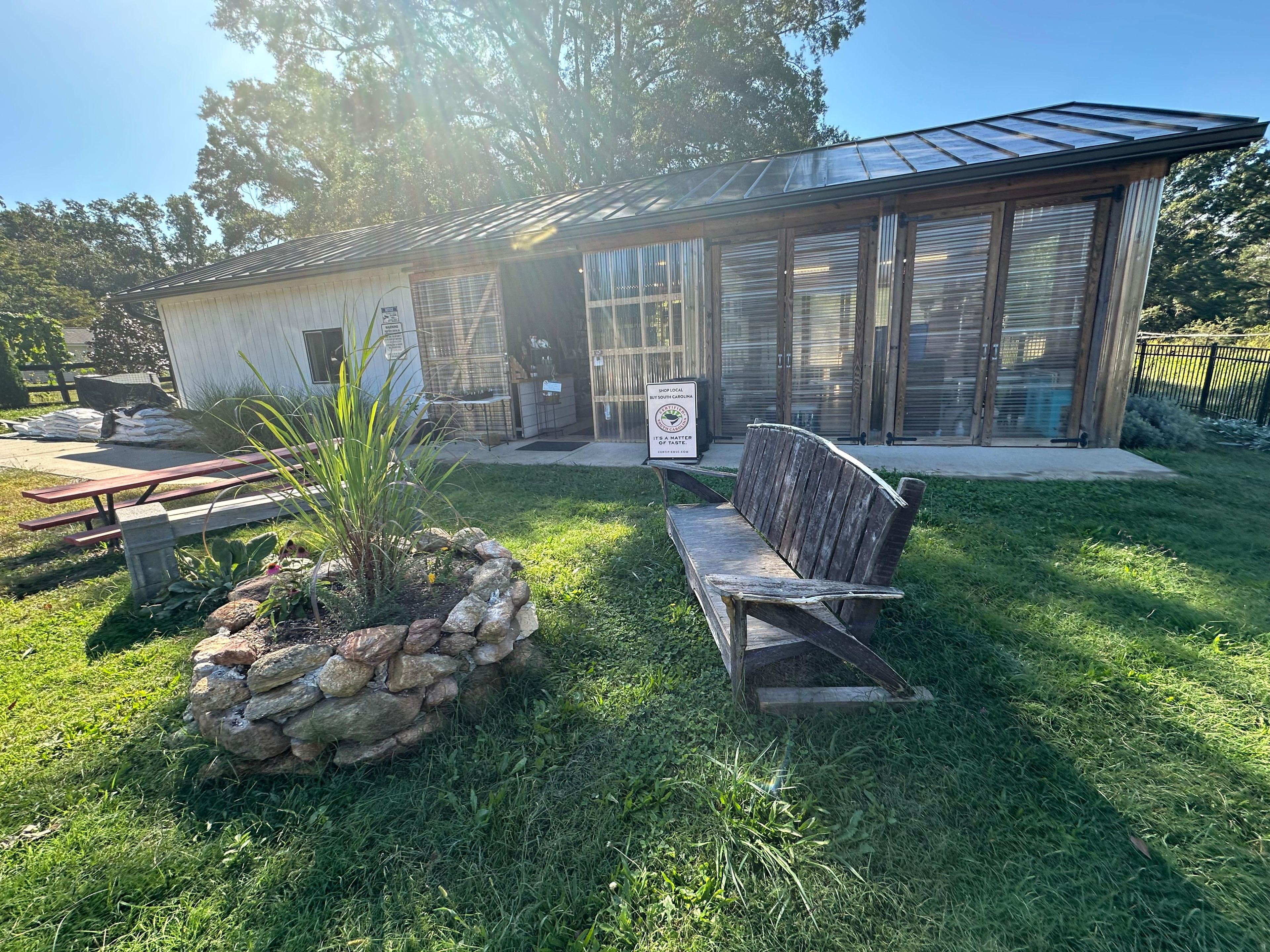 A building with a stone wall, a wooden bench, and a picnic table in a grassy area.