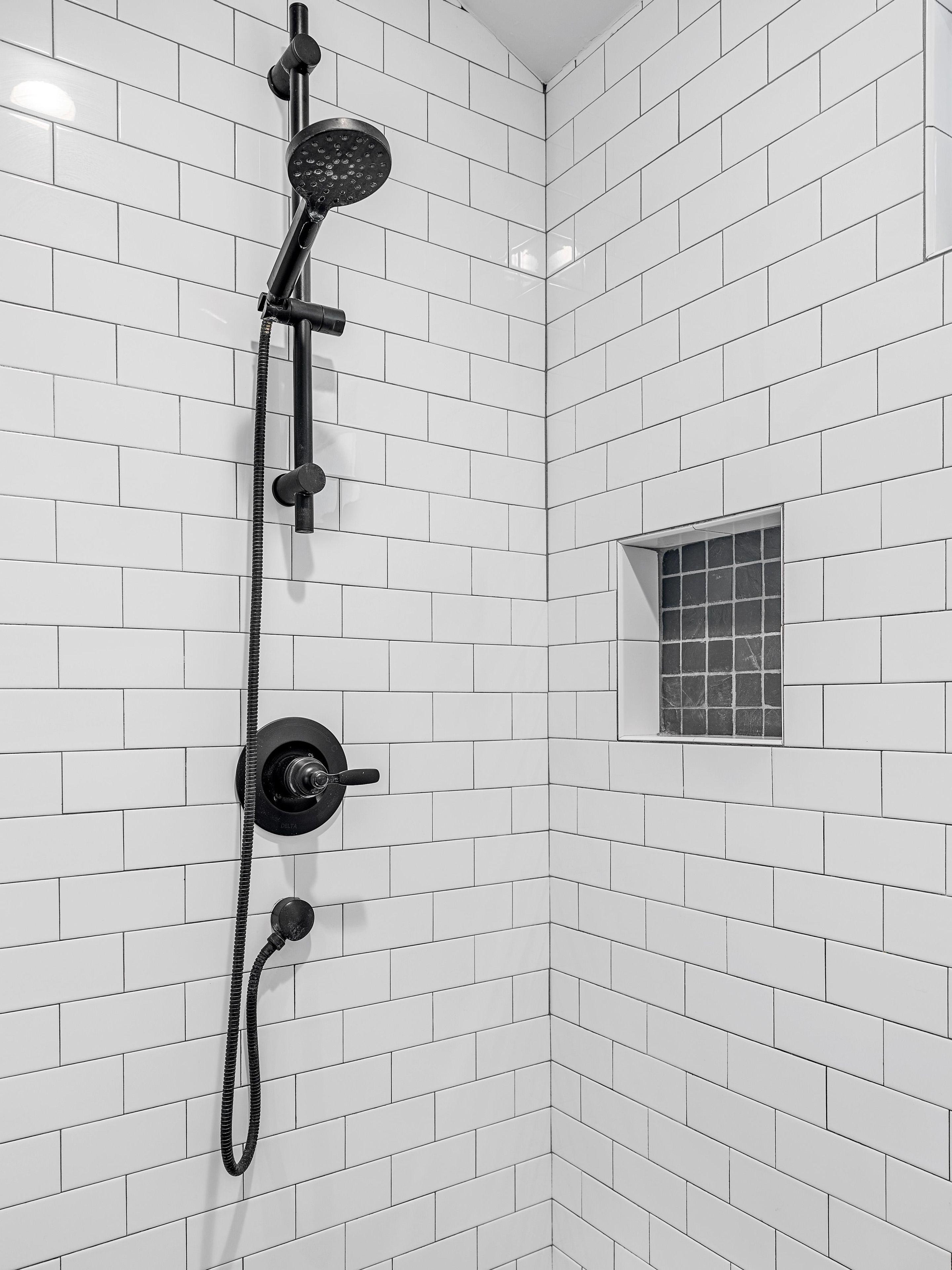 Eine Dusche mit Handbrause und fest installierter Duschbrause, beide mit schwarzen Schläuchen.
