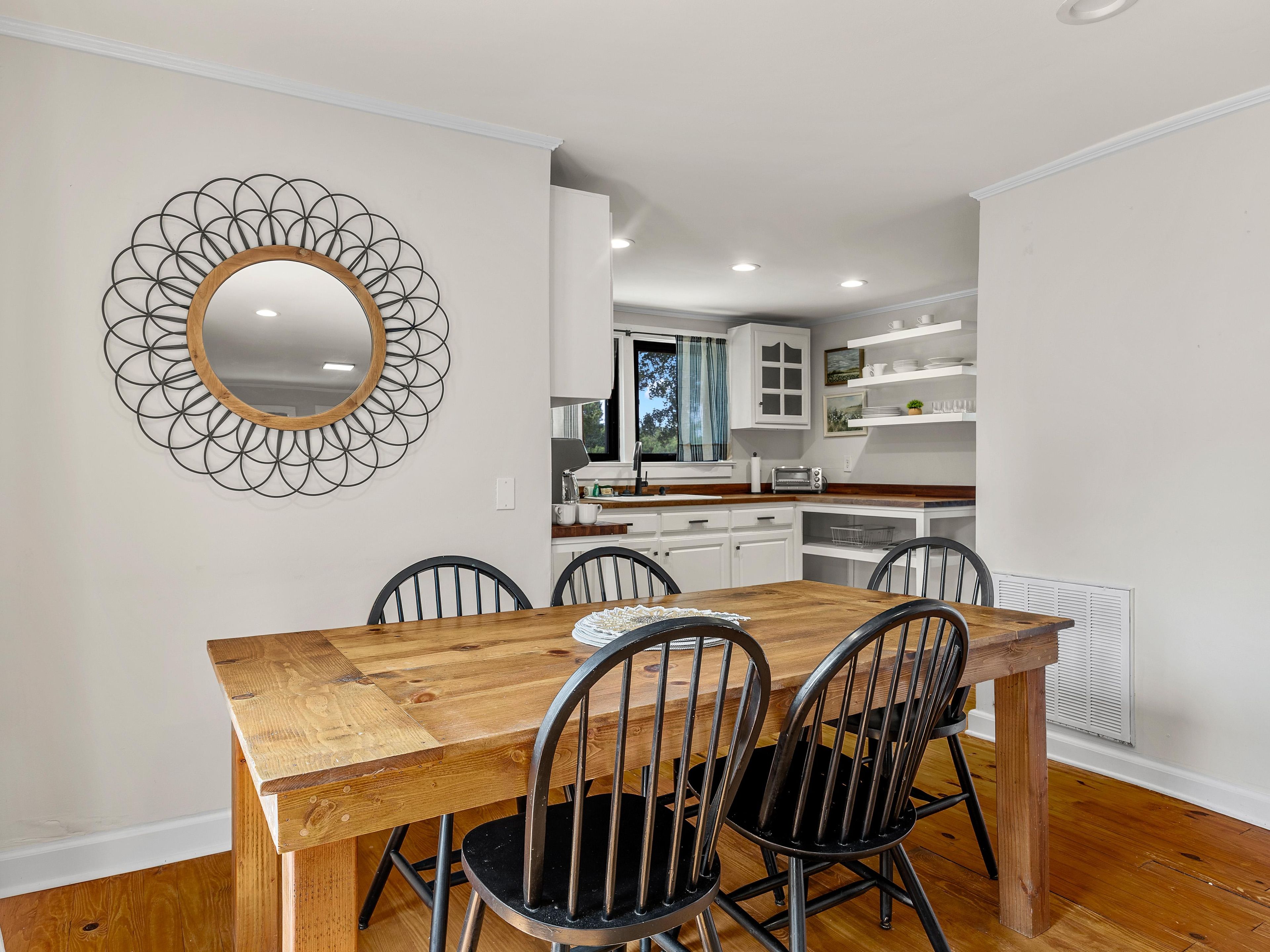 A dining area with a wooden table and chairs, a decorative mirror, and a kitchen in the background.