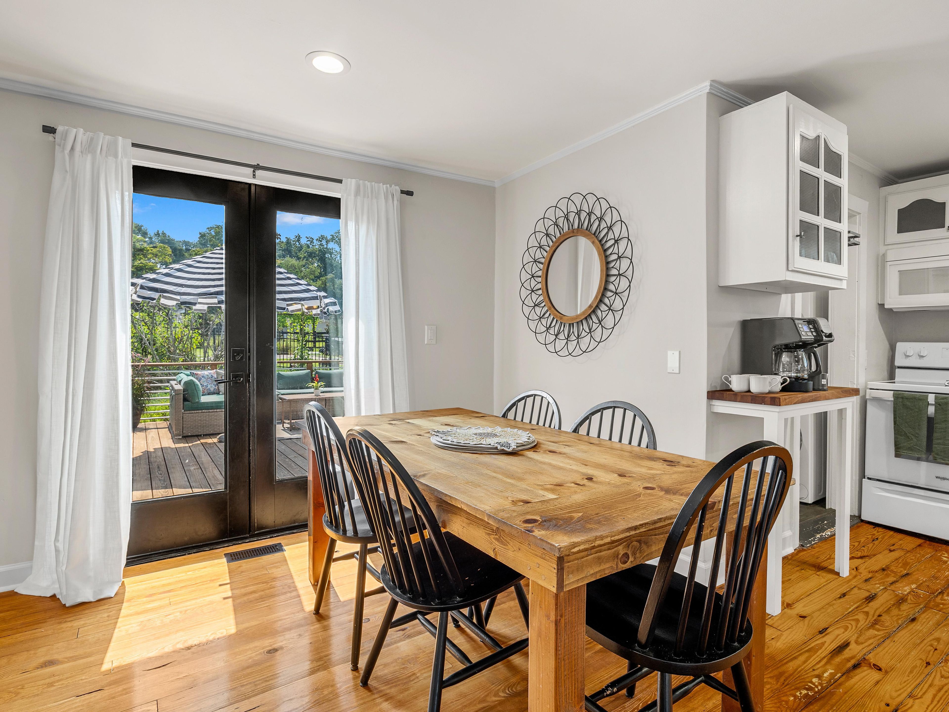 A dining area with a wooden table and chairs, a kitchen with white cabinets, and a view of the outdoors through a sliding door.