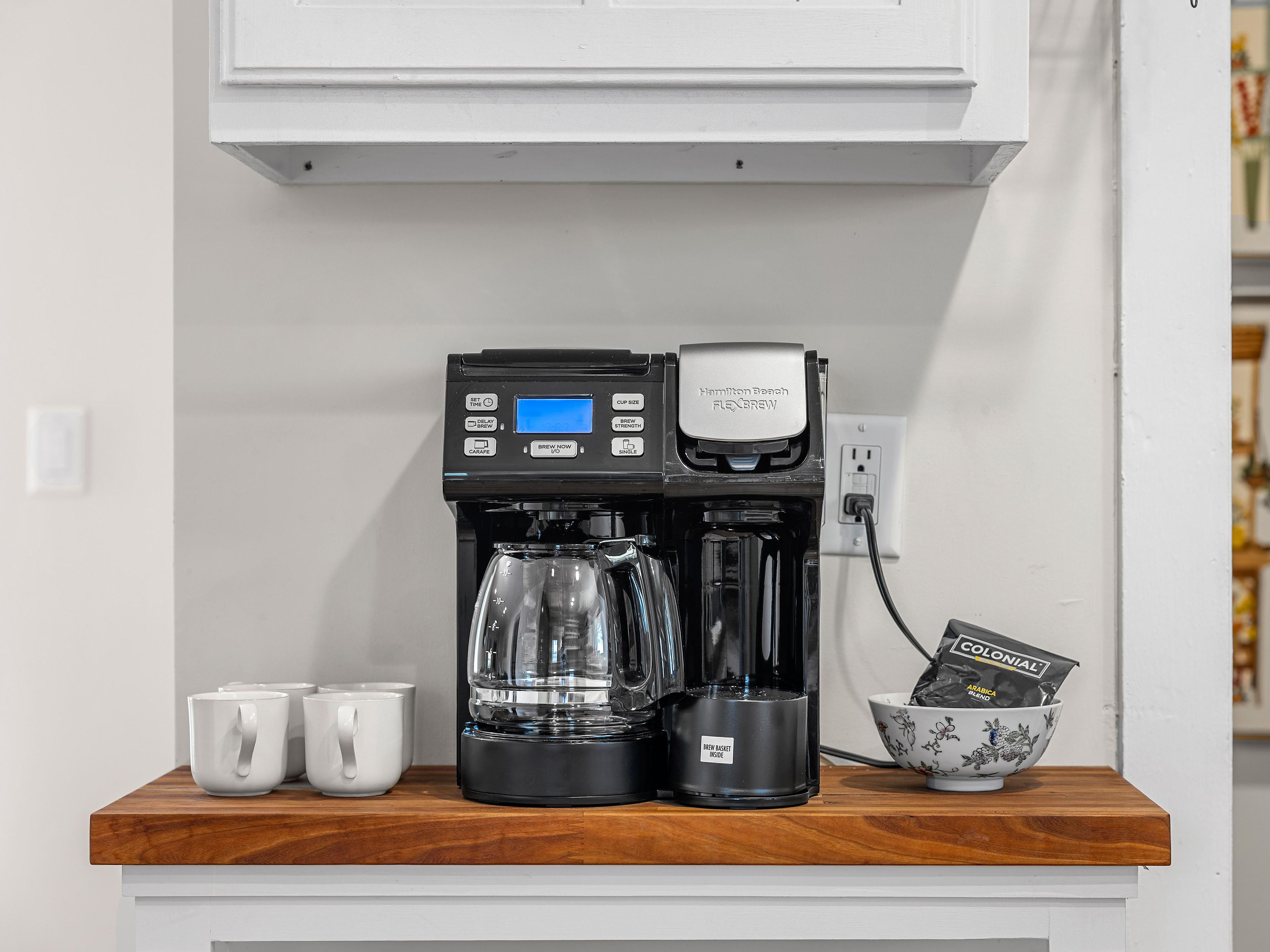 Eine Kaffeemaschine auf einer Holzausstellung mit Kaffeekanne und Kapselbehälter.