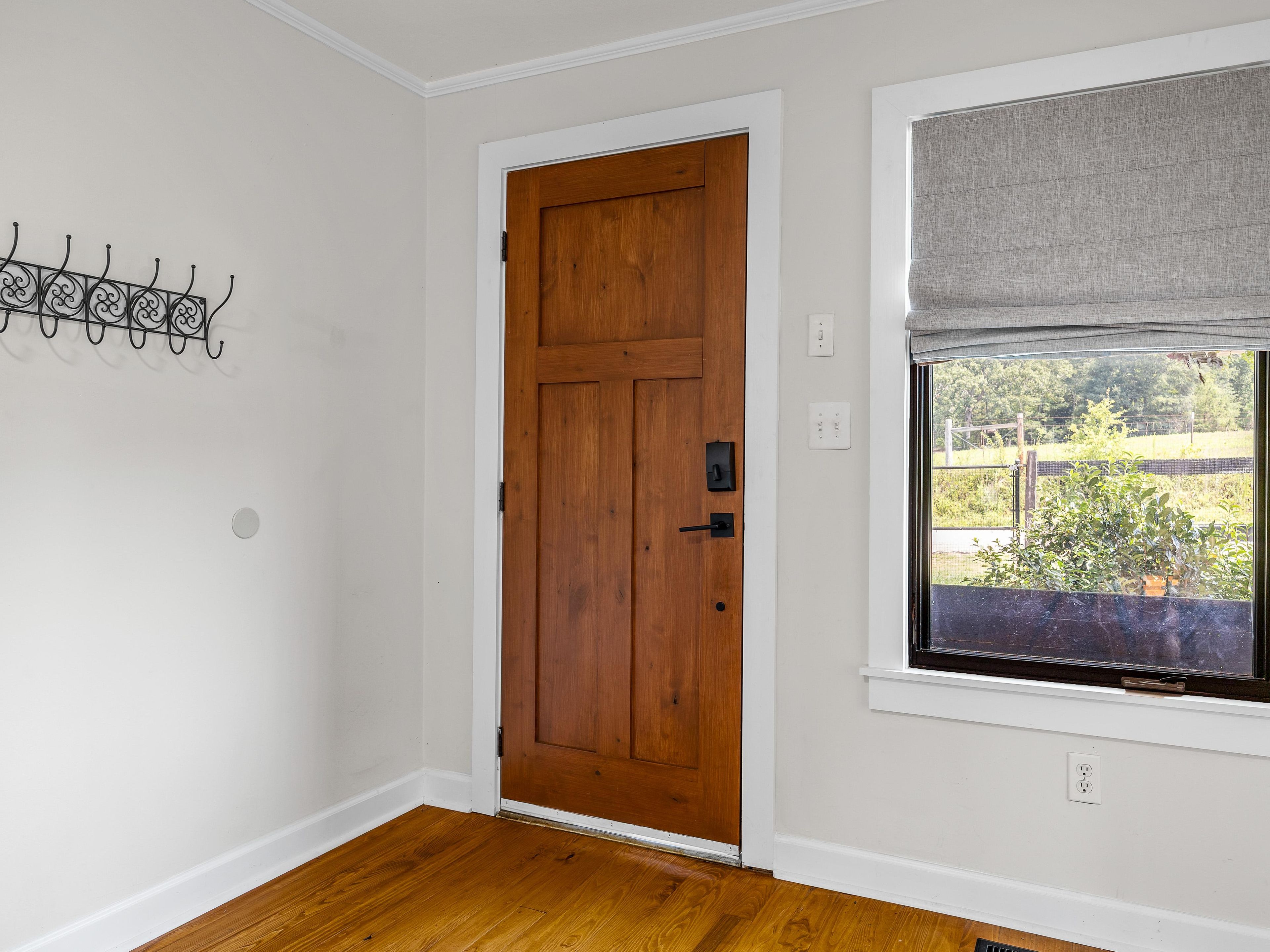 Ein Zimmer mit Holztür, einem Fenster mit Ausblick und einem an der Wand befestigten Lichtschalter.