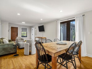 Ein Essbereich mit Holztisch und -stühlen, einem an der Wand befestigten Fernseher und Blick ins Freie durch ein großes Fenster.