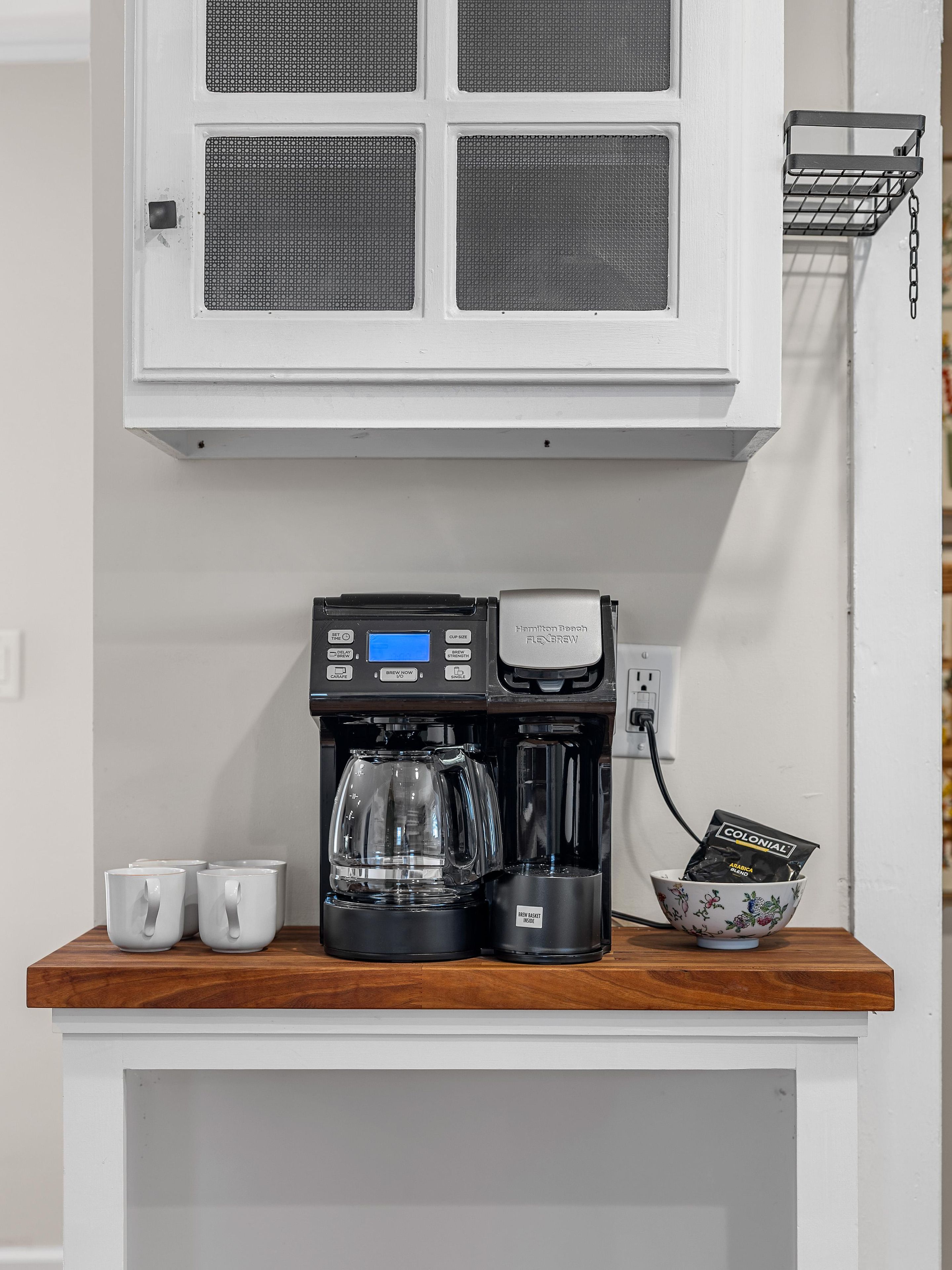 A coffee maker on a wooden countertop with a white cabinet above it.