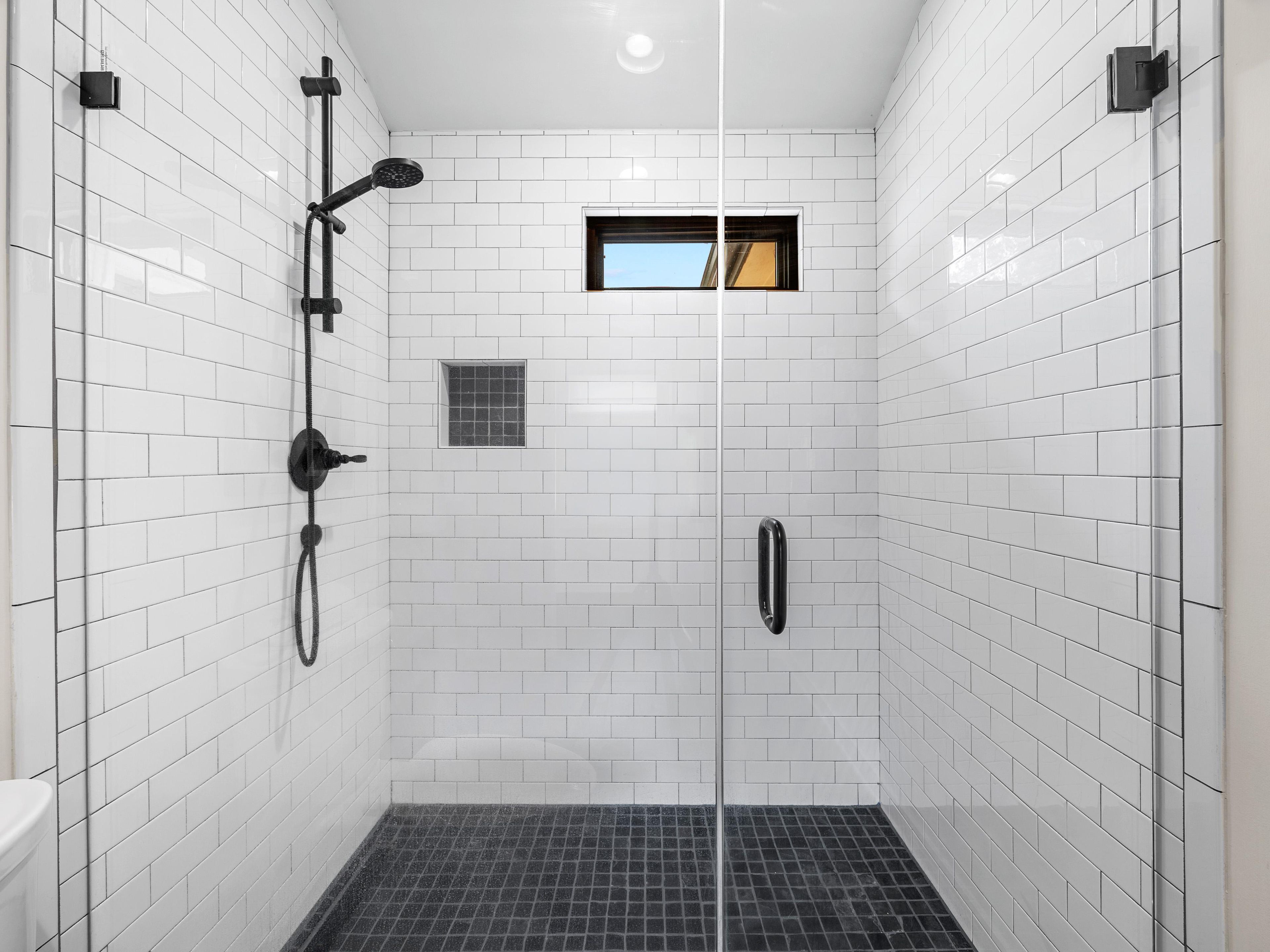 A modern shower with white tiles, a glass door, and a black floor.