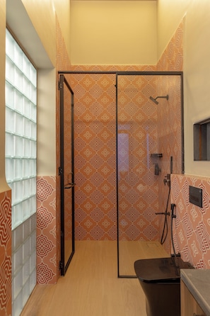 A shower room with a glass door, a shower head, and a control panel.