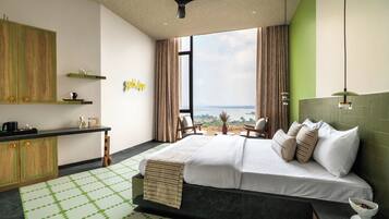 A modern hotel room with a large bed, a desk, a view of the sea, and a ceiling fan.
