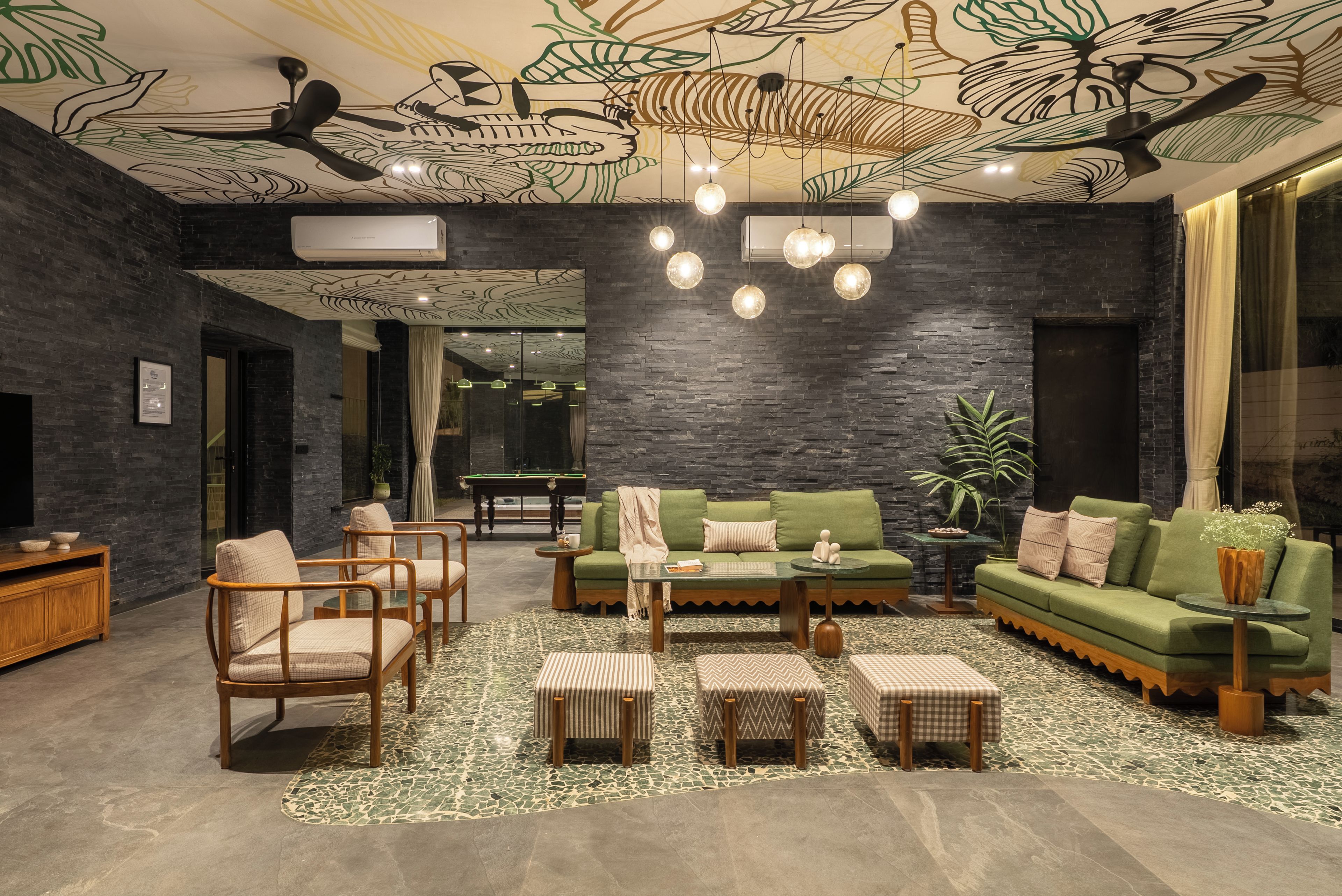 A modern lounge with a pool table, green sofas, and a ceiling with leaf patterns.