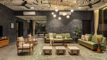A modern lounge with a pool table, green sofas, and a ceiling with leaf patterns.