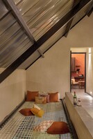 Un dormitorio acogedor en el ático, con techo inclinado, una cama con ropa de cama estampada y una pequeña mesa con una botella y un vaso.