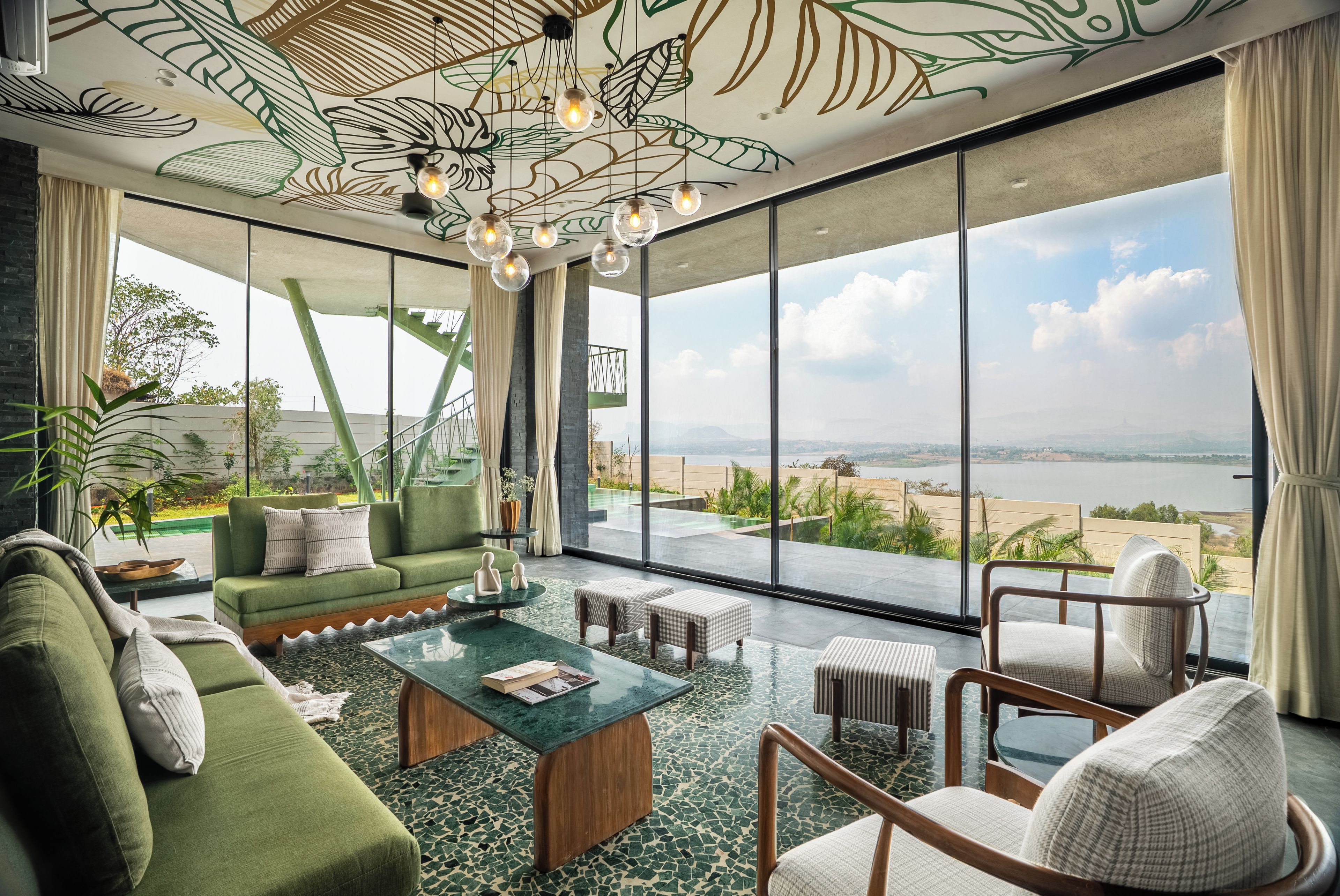 A spacious living room with a green sofa, a coffee table, and a view of a beach and ocean through large windows.