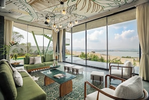 A spacious living room with a green sofa, a coffee table, and a view of a beach and ocean through large windows.
