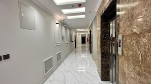 A hotel corridor with a marble floor, recessed lighting, and a marble wall.