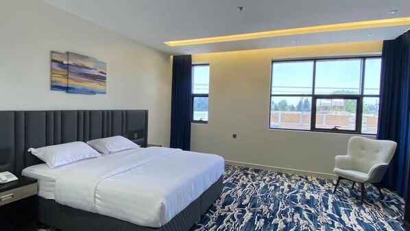 Quarto de hotel com cama grande, uma cadeira, escrivaninha com telefone e janela com vista.