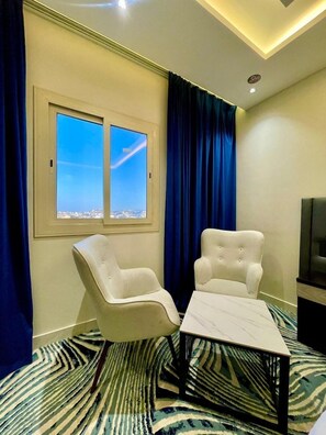 A room with two white armchairs, a small table, a television, and a window with a view of a cityscape.