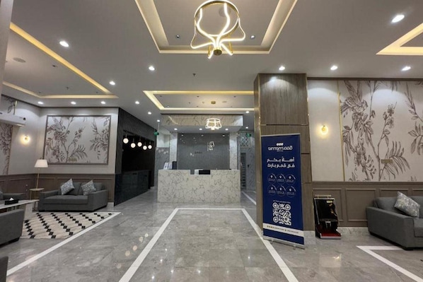 A hotel lobby with a reception desk, seating area, and a decorative wall with floral patterns.