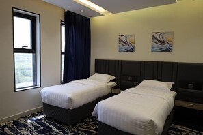 Quarto de hotel com duas camas, uma janela grande e arte abstrata nas paredes.