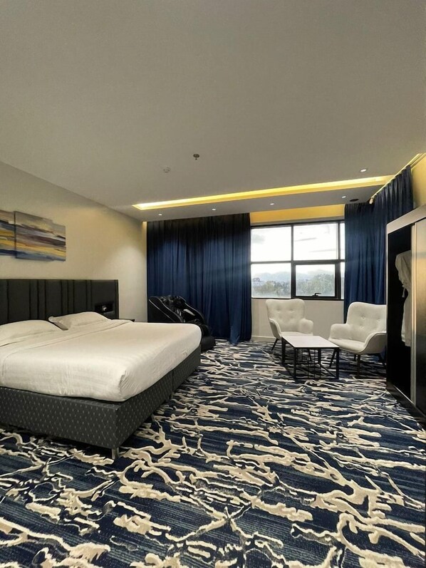 A hotel room with a large bed, a seating area with two chairs, a wardrobe, and a window with curtains.