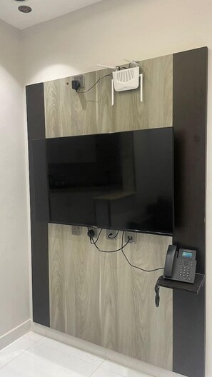 A wall-mounted flat-screen TV with a telephone and a small white device on a wall with wood paneling.