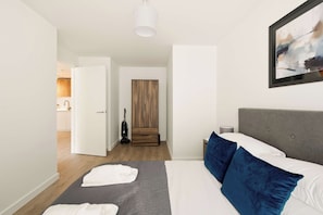 A modern hotel room with a bed, a painting, and a hallway leading to a bathroom. - Modern & Bright 1BED Central Birmingham Apartment (Birmingham)