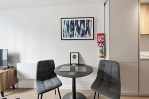 A modern room with a round table, two grey chairs, a framed abstract painting, a fire extinguisher, and a television on a wooden cabinet. - Modern & Bright 1BED Central Birmingham Apartment (Birmingham)