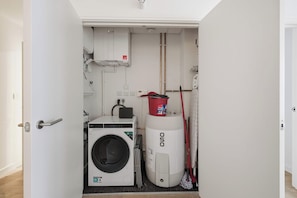A laundry room with a front-loading washing machine, a dryer, and a mop. - Modern & Bright 1BED Central Birmingham Apartment (Birmingham)