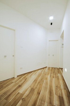 A hallway with wooden flooring, white walls, and doors leading to other rooms. - Lara's Home (Naples)