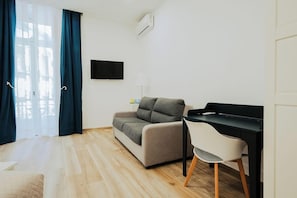 A modern room with a sofa, a desk with a chair, a flat-screen TV, and an air conditioning unit. - Lara's Home (Naples)