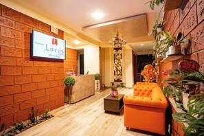 A reception area with a brick wall, a reception desk, a sofa, and potted plants. - Gaurav Lords Resort (Shrivardhan)