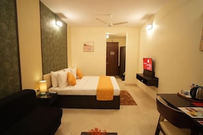 A hotel room with a bed, a desk, a chair, a TV, and a ceiling fan. - Gaurav Lords Resort (Shrivardhan)