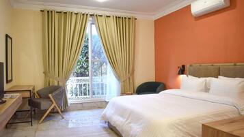 A hotel room with a bed, a desk, a chair, and a window with curtains.