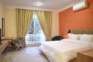 Una habitación de hotel con cama, escritorio, silla y ventana con cortinas.