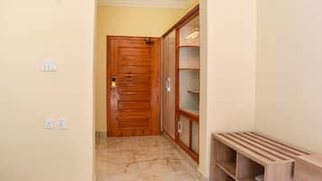 Un pasillo con puerta de madera, suelo de baldosas de mármol y estantería de madera.