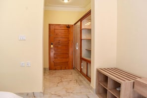 A hallway with a wooden door, a marble-tiled floor, and a wooden shelving unit.