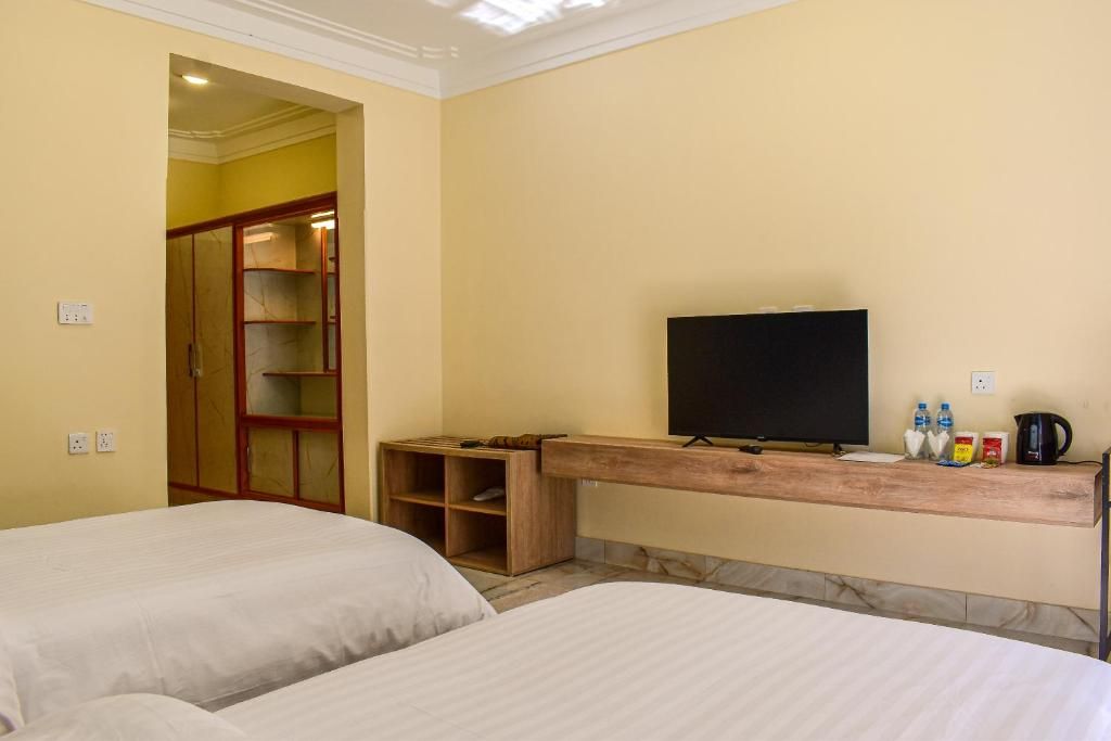 A hotel room with two beds, a television, a wooden shelf with items, and a wardrobe.
