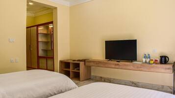 A hotel room with two beds, a television, a wooden shelf with items, and a wardrobe.